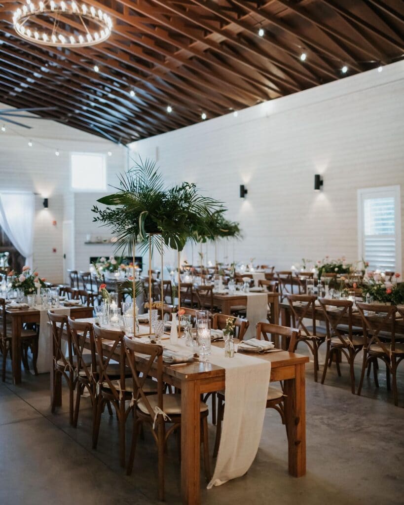 interior of white barn with wood rafters and large round chandelier with tables and chairs set up for wedding reception